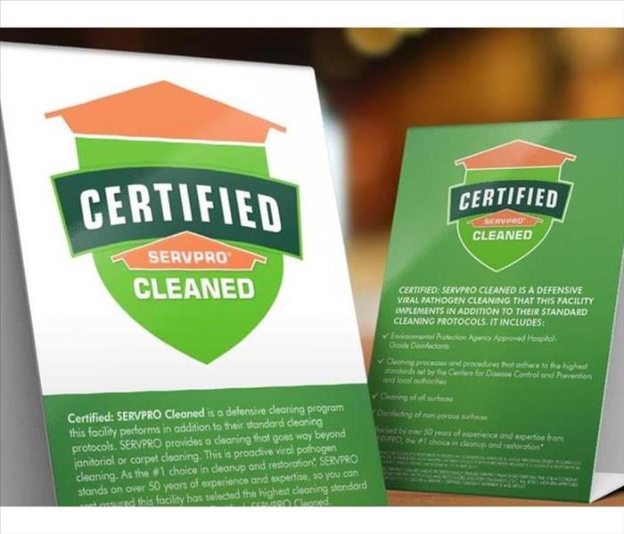 Table tent signs describing the Certified: SERVPRO Cleaned programon top of a wooden table. 